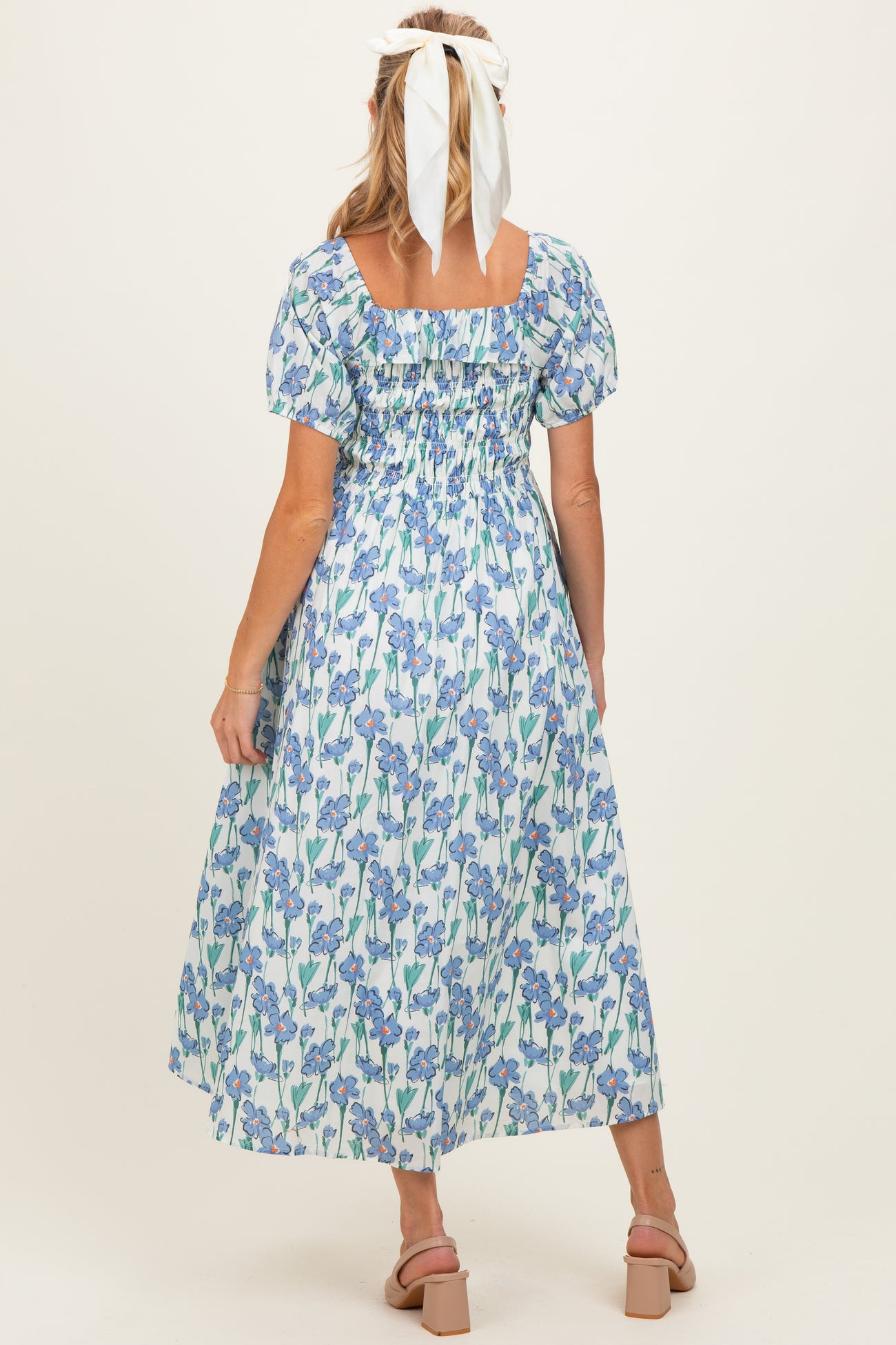 woman wearing a floral maternity dress with puff sleeves and a square neckline, showing her back and long flowy skirt