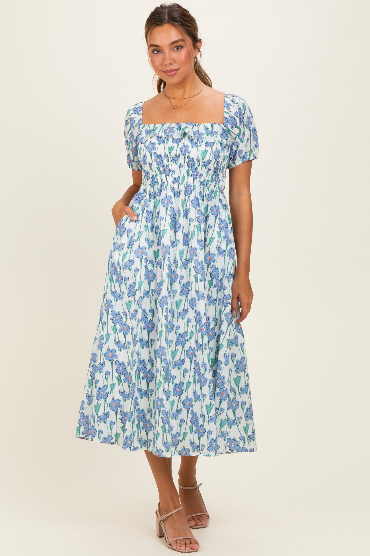 woman wearing a floral print midi dress with a square neckline and puff sleeves, standing with hands in pockets