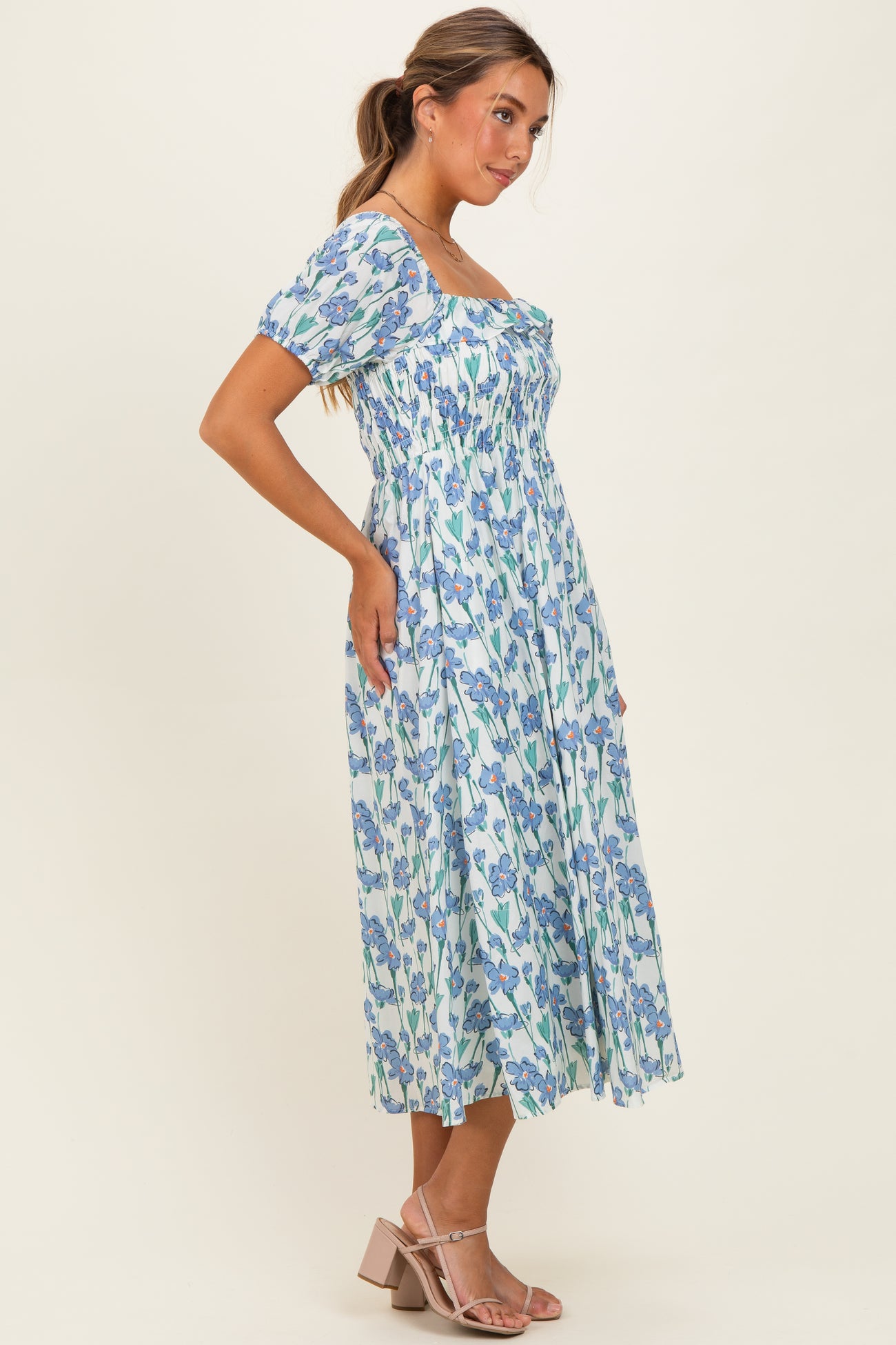 woman wearing a floral midi dress with puff sleeves and a fitted bodice, standing sideways against a light background