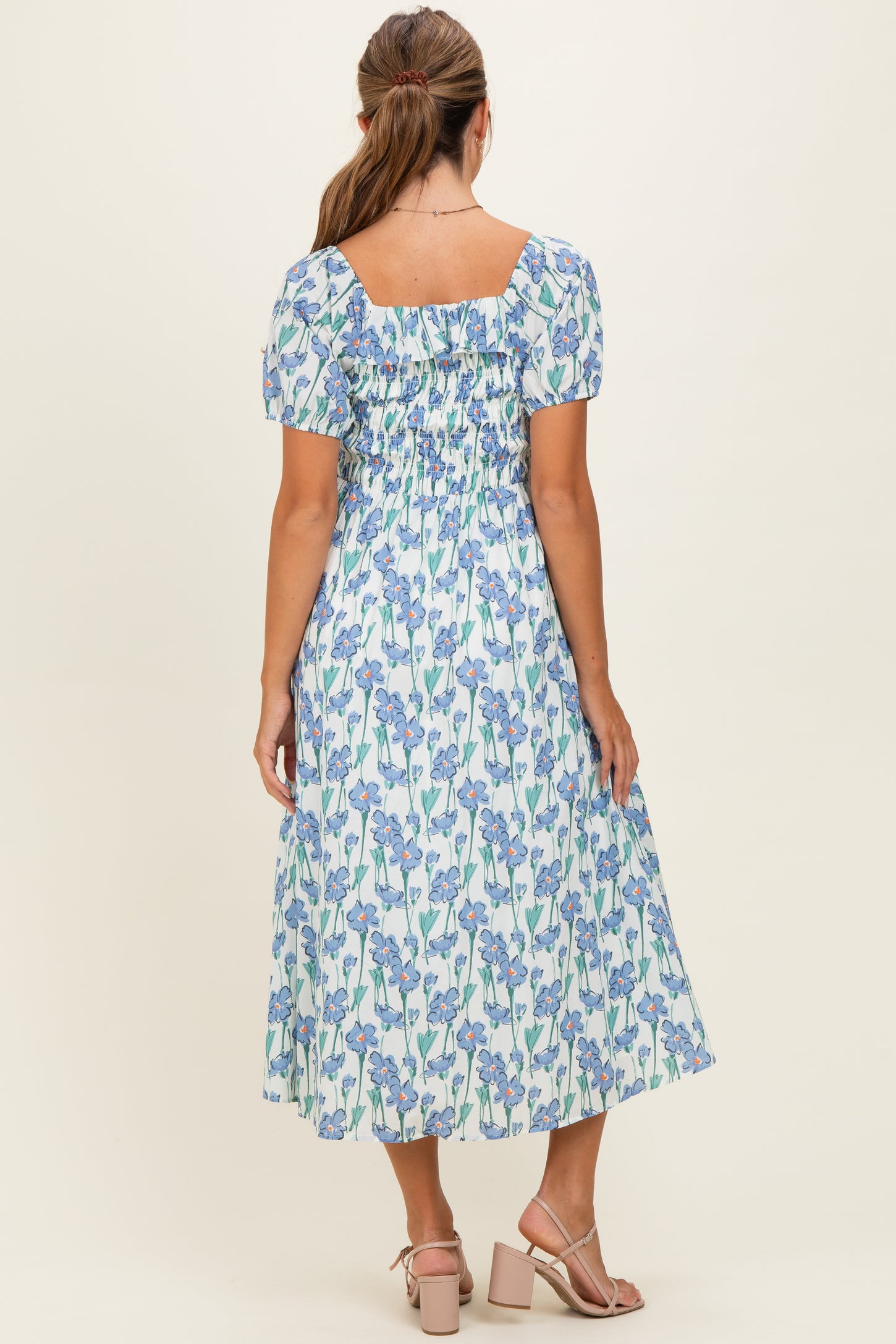 woman wearing a blue floral midi dress with short puff sleeves and a smocked back, standing with her back to the camera