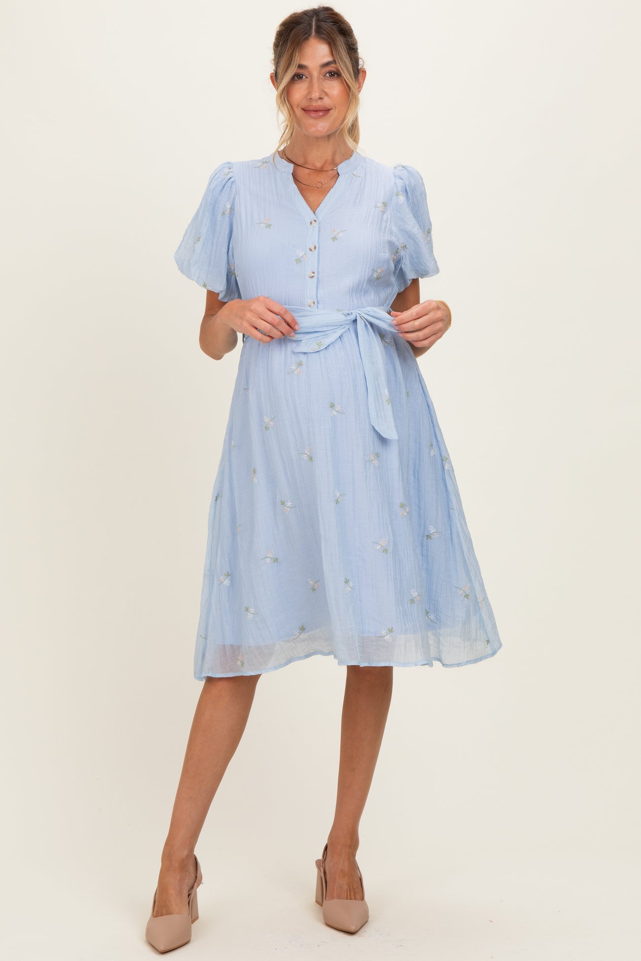 woman wearing a light blue short sleeve maternity dress with buttons and a tie waist, featuring floral embroidery