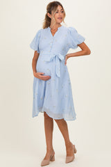 woman wearing a light blue maternity dress with puff sleeves and floral details, holding her baby bump