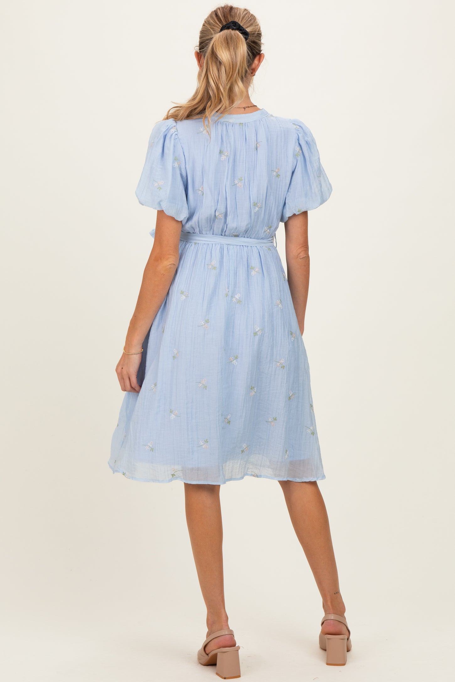 woman wearing a light blue maternity dress with puff sleeves and floral embroidery, showing a relaxed fit and cinched waist
