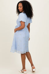 woman wearing a light blue short sleeve embroidered dress with a cinched waist and skirt detail, viewed from the back