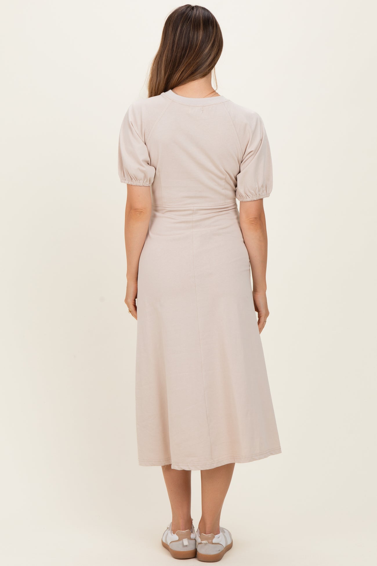 woman wearing a light beige puff sleeve maternity dress, view from the back, with a flowy midi length
