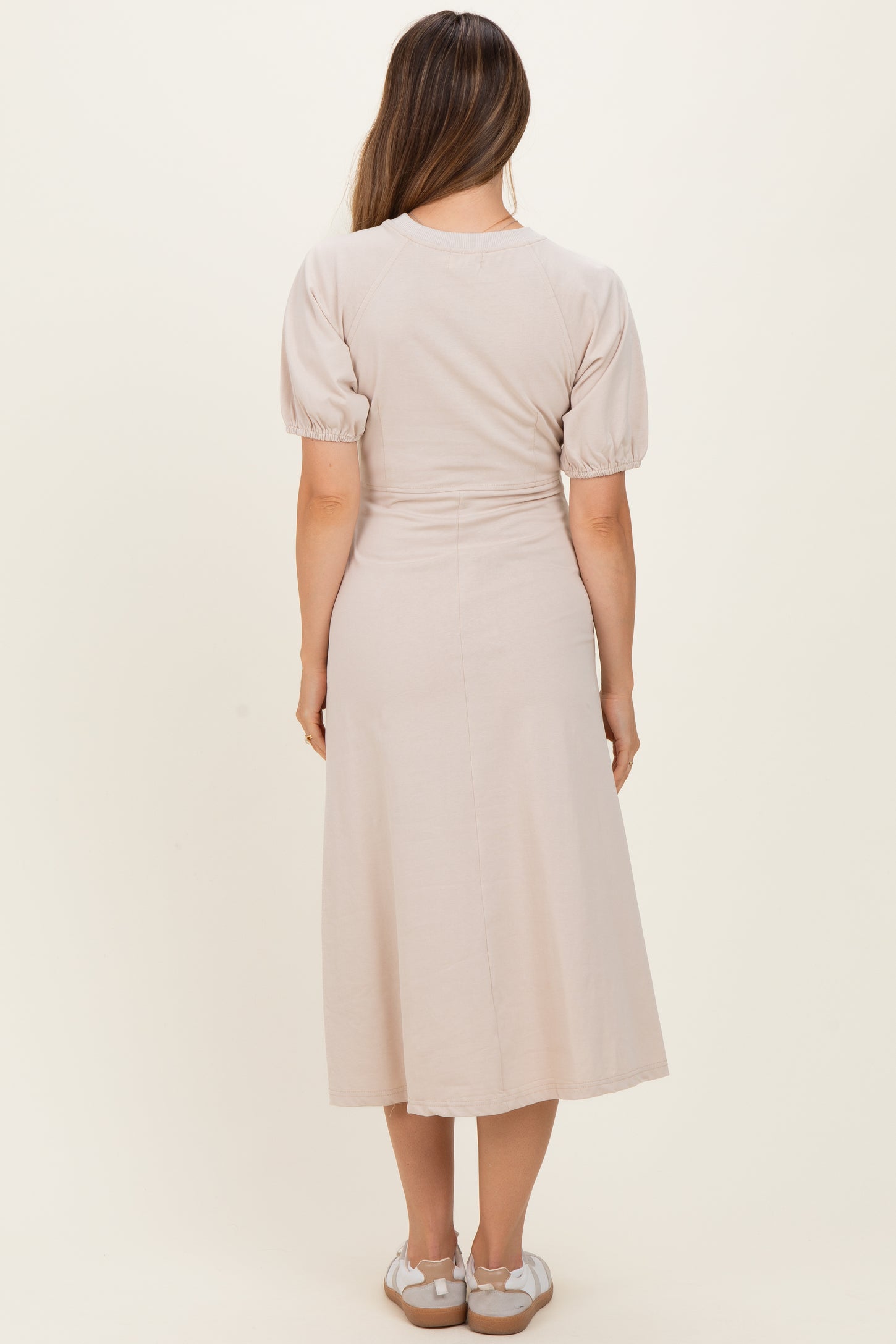 woman wearing a light beige puff sleeve maternity dress, view from the back, with a flowy midi length