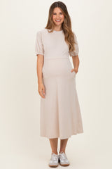 woman wearing a beige maternity midi dress with puff sleeves and pockets