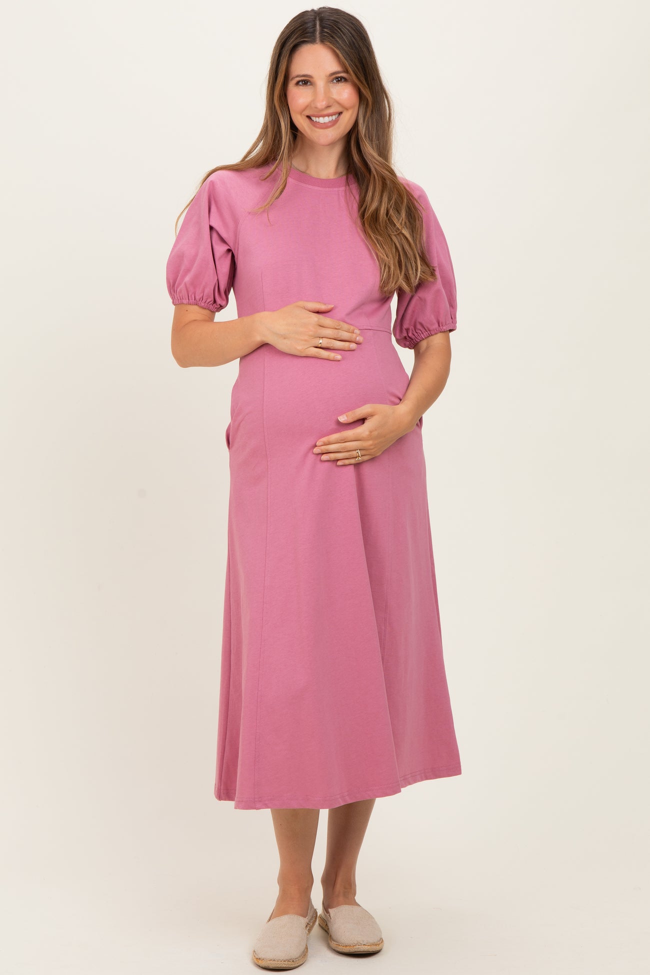 woman wearing a pink short sleeve maternity dress and holding her baby bump
