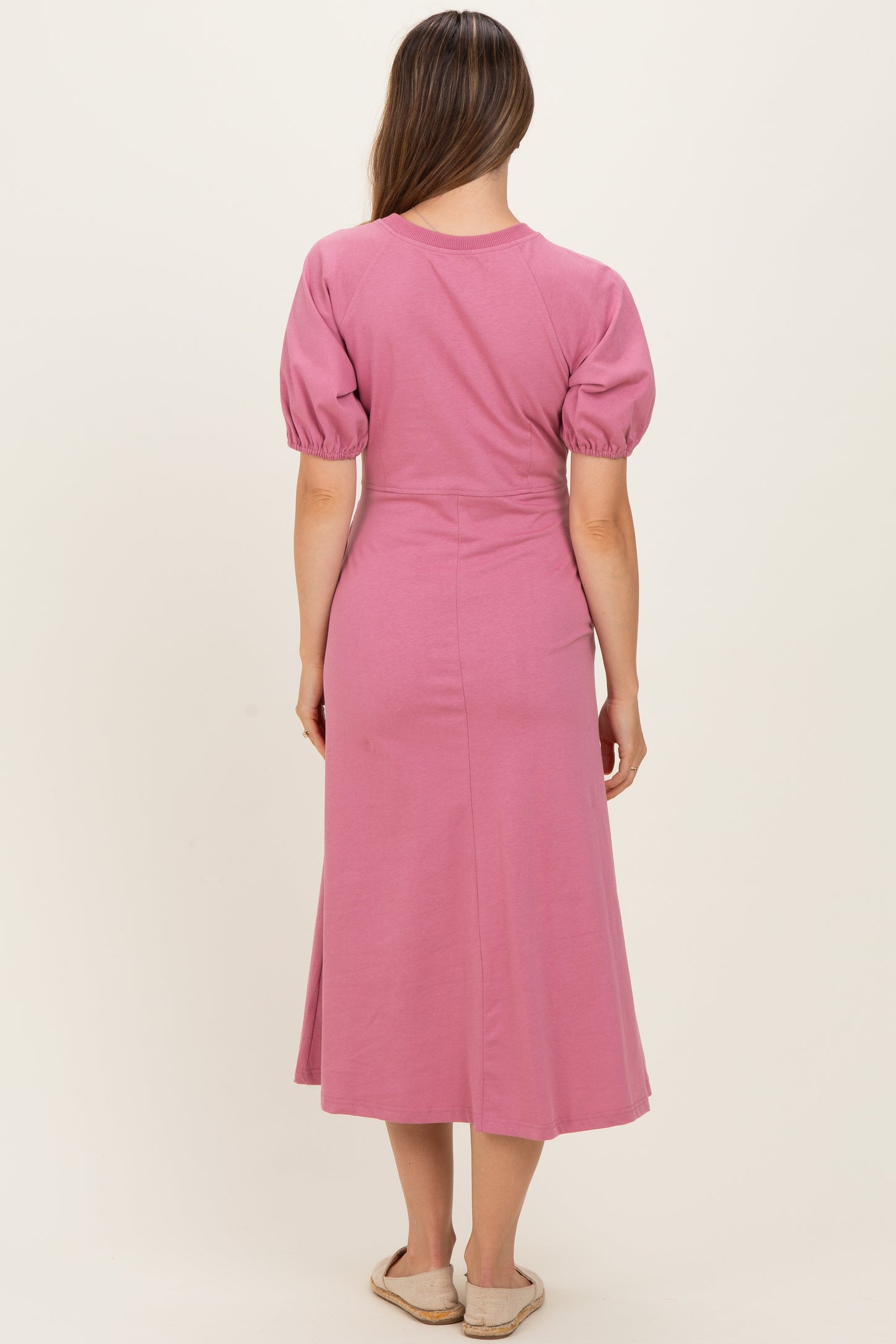 woman wearing a pink maternity dress with puff sleeves and a midi length, view from the back