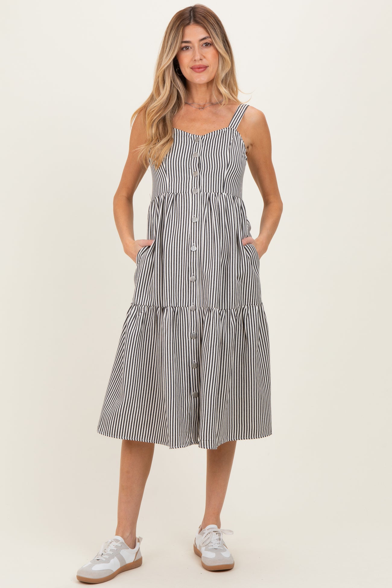 woman wearing a striped maternity sundress with pockets and buttons, standing in casual sneakers