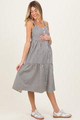 woman wearing a black and white striped maternity dress with buttons, gently cradling her baby bump