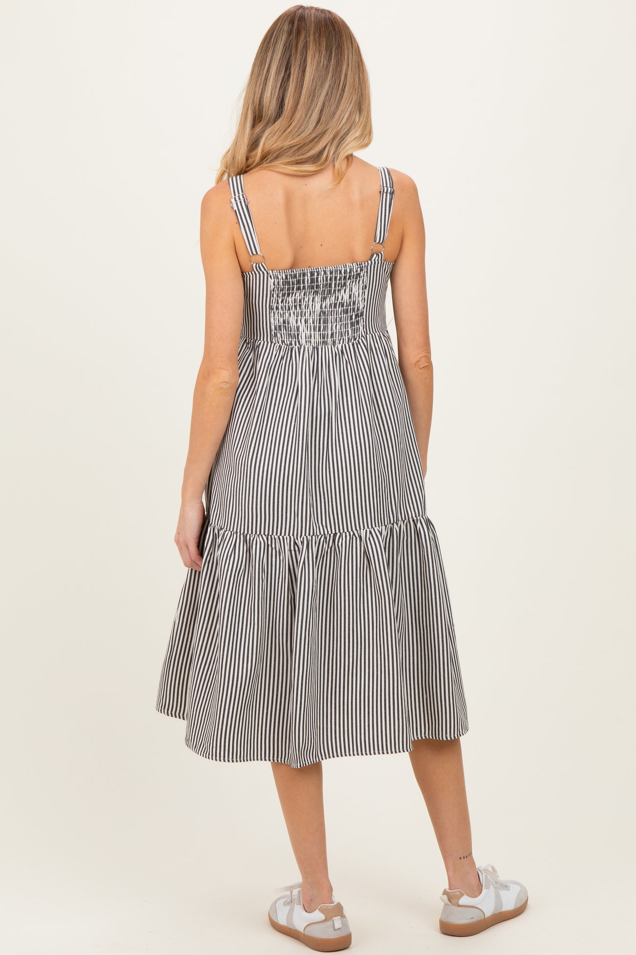 woman wearing a black and white striped maternity midi dress with adjustable straps and a smocked back