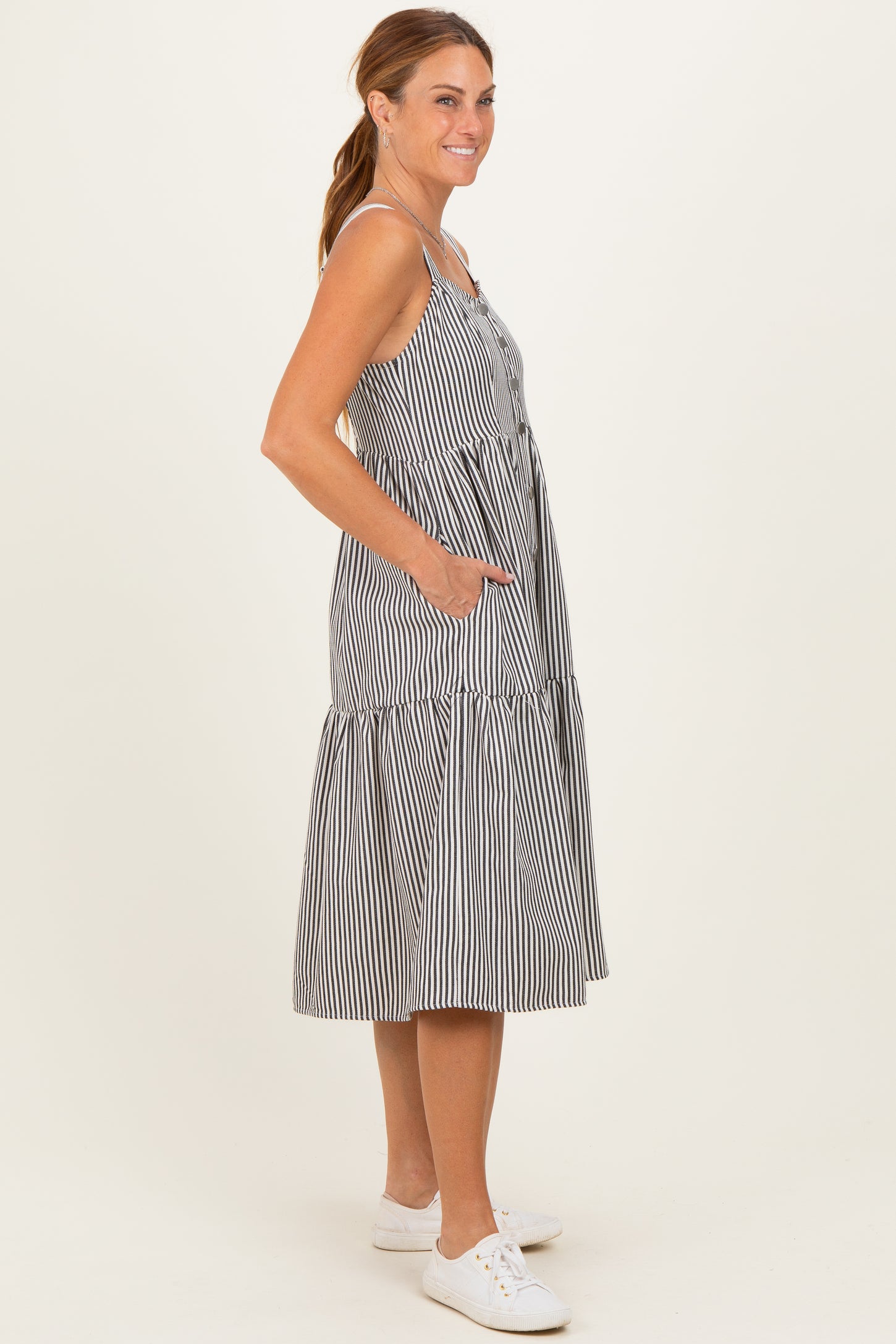 woman wearing a black and white striped midi dress with button details and side pockets, standing sideways