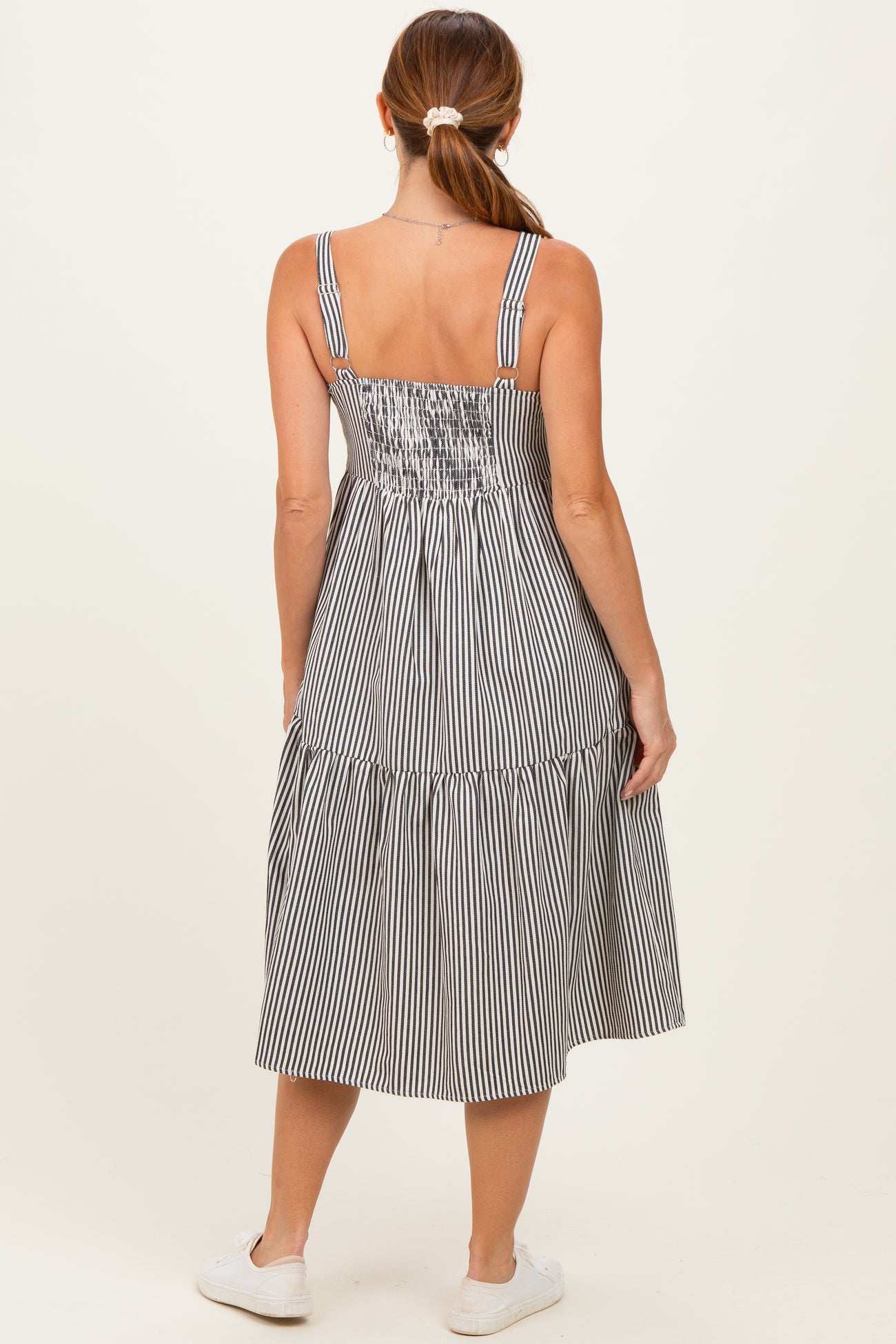 woman wearing a striped midi dress with spaghetti straps and a tiered skirt, viewed from the back