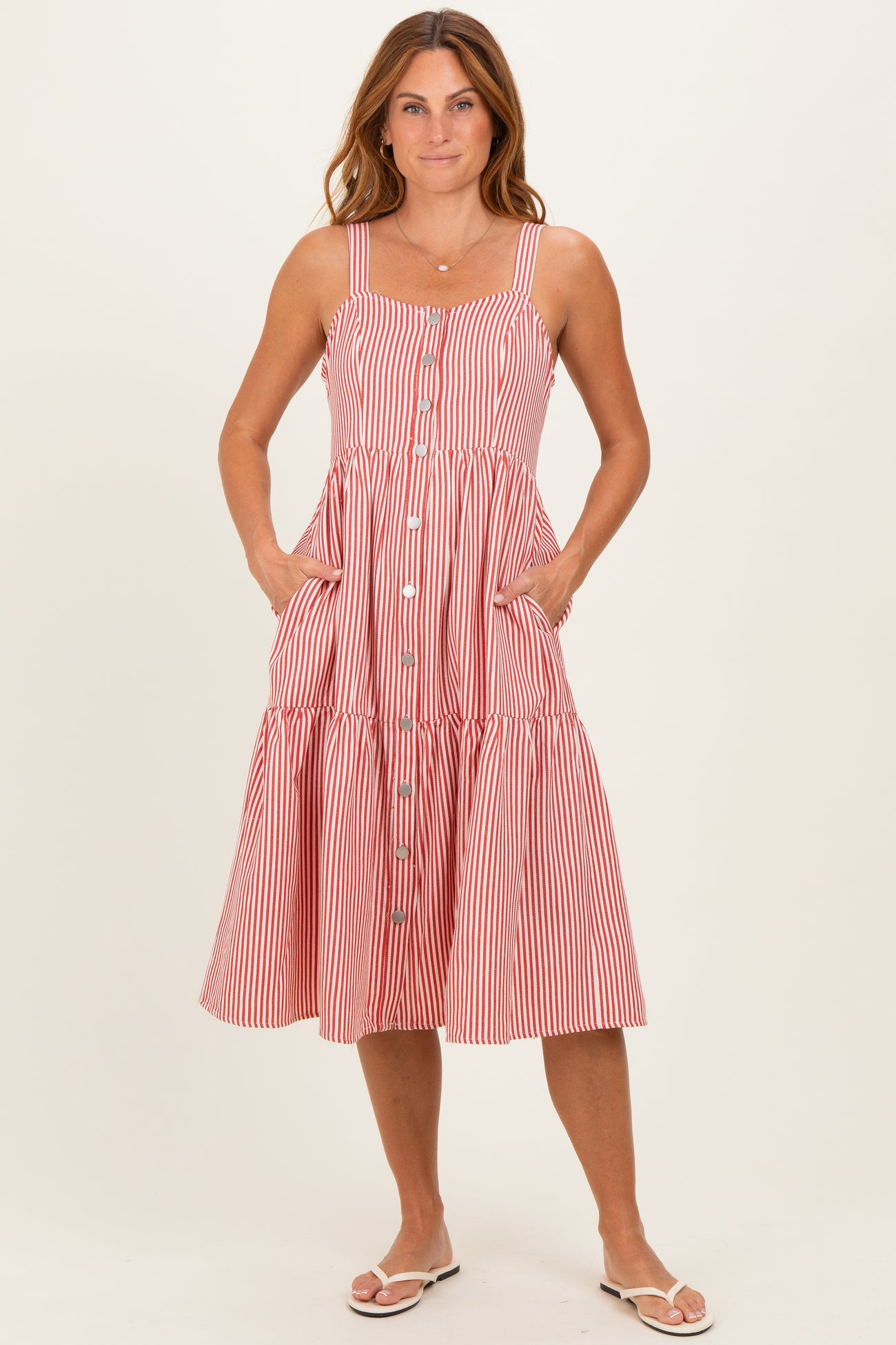 woman wearing a red and white striped sundress with a button-down front and pockets, standing with hands in pockets