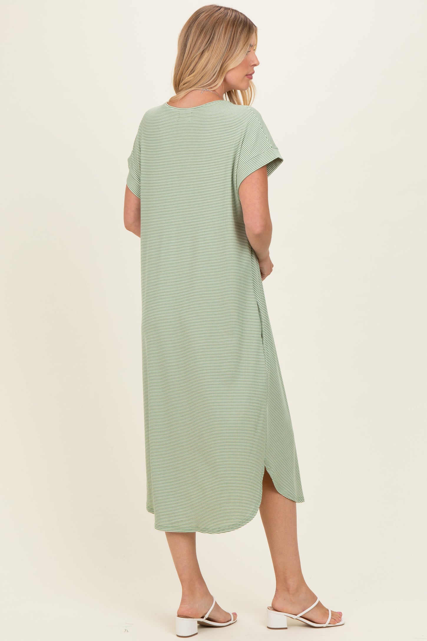 woman wearing a green maxi dress with short sleeves and side slits, standing with her back to the camera