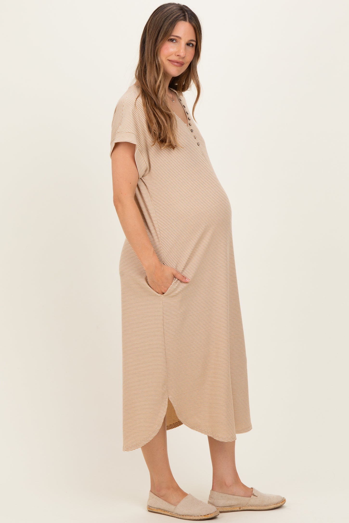 woman wearing a beige striped short sleeve maternity dress with pockets and a visible baby bump