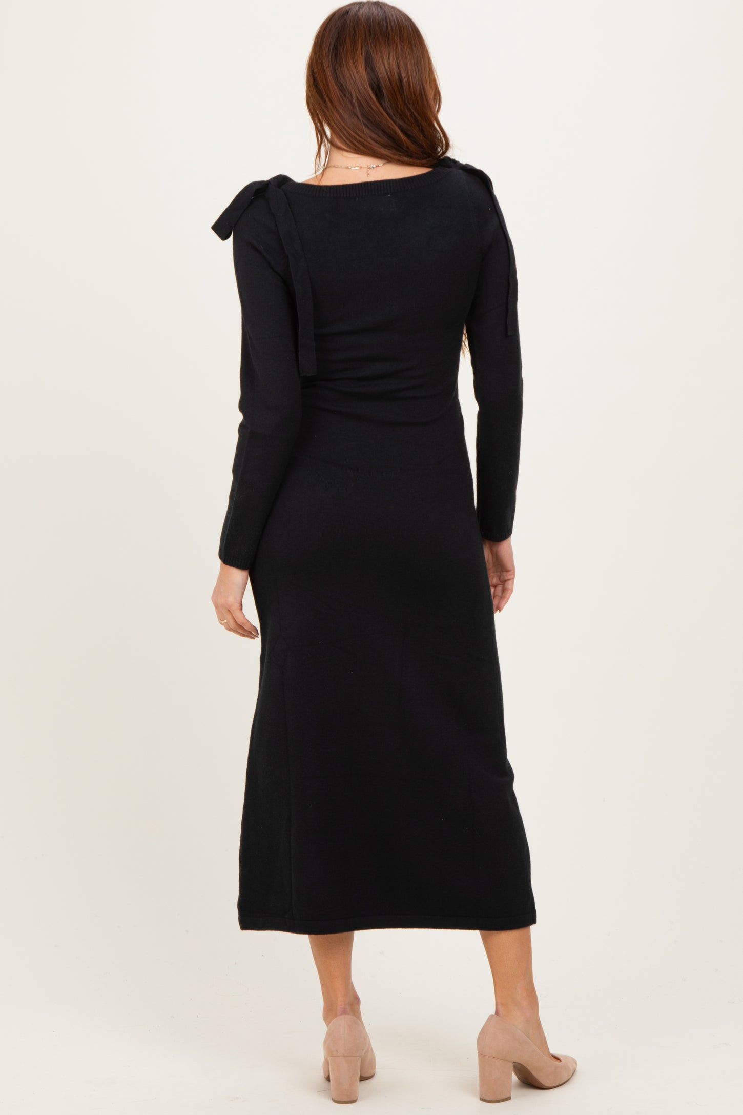 woman wearing a black long sleeve dress with shoulder ties and a fitted silhouette, seen from the back