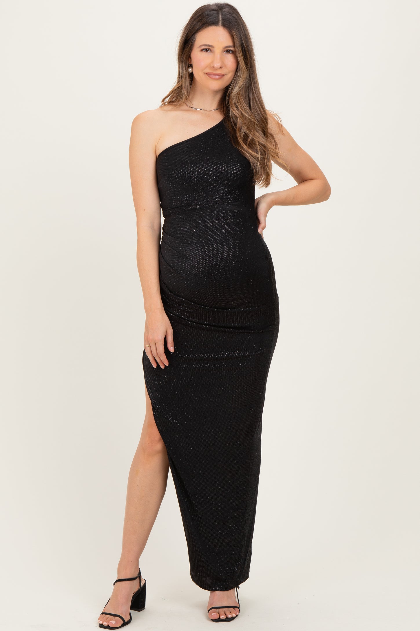 woman wearing a black one-shoulder sequined maternity gown with a side slit and showing a baby bump