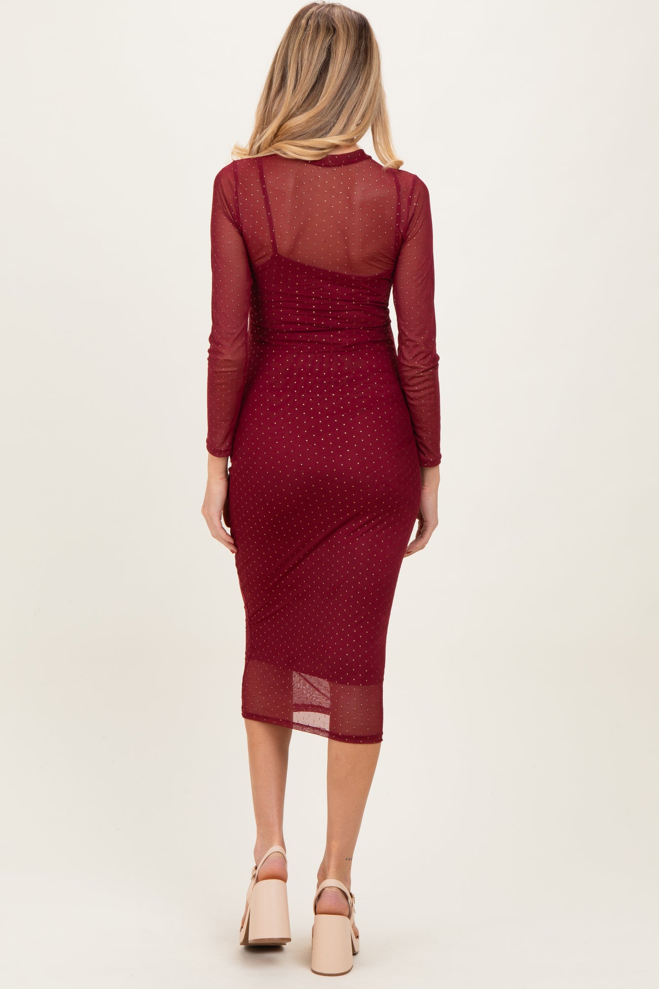 woman wearing a burgundy maternity midi dress with long sleeves and sheer back, showcasing her baby bump