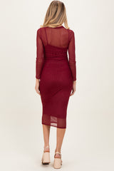 woman wearing a burgundy maternity midi dress with long sleeves and sheer back, showcasing her baby bump
