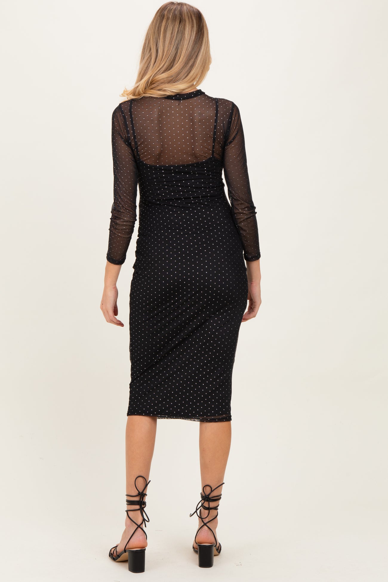 woman wearing a black maternity dress with a sheer dotted overlay and fitted silhouette