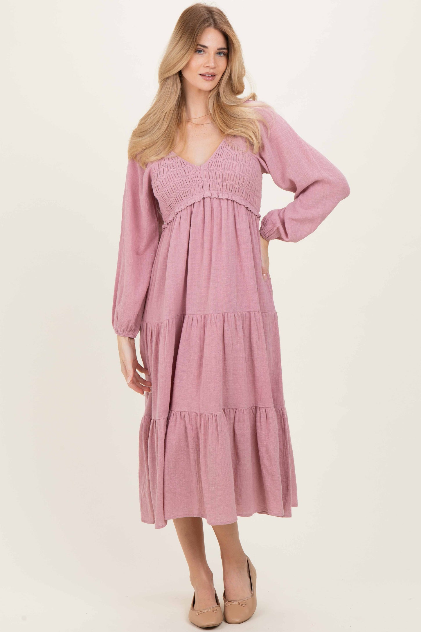woman wearing a light pink long sleeve tiered maxi dress with a smocked bodice and a v-neckline