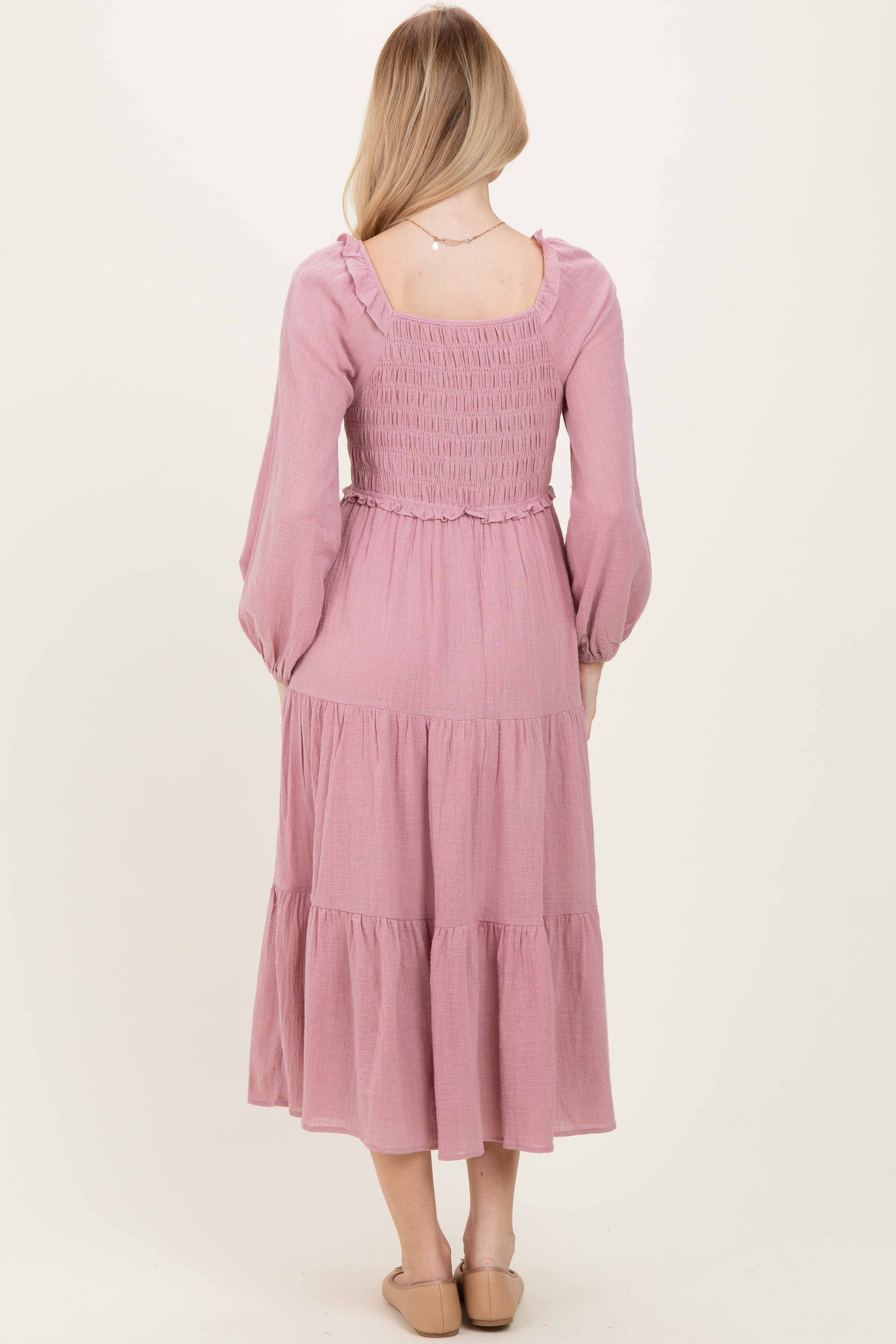 woman wearing a light pink long sleeve tiered maxi dress with a smocked back and ruffled details.