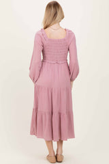 woman wearing a light pink long sleeve tiered maxi dress with a smocked back and ruffled details.