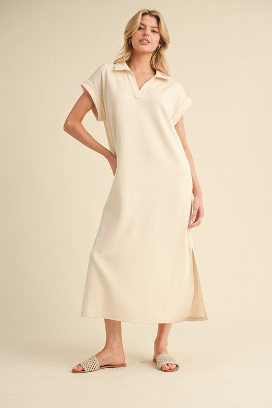 woman wearing a beige short sleeve polo-style dress with a side slit and standing in slide sandals