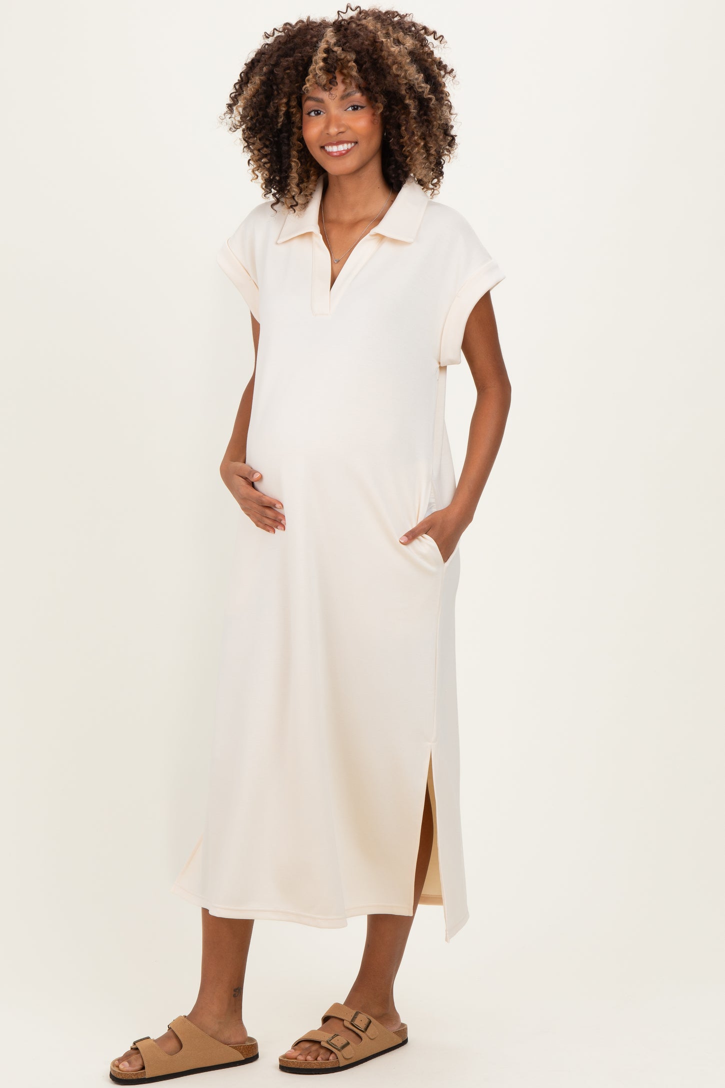 woman wearing a light peach maternity dress with short sleeves, side slits, and pockets, highlighting her baby bump