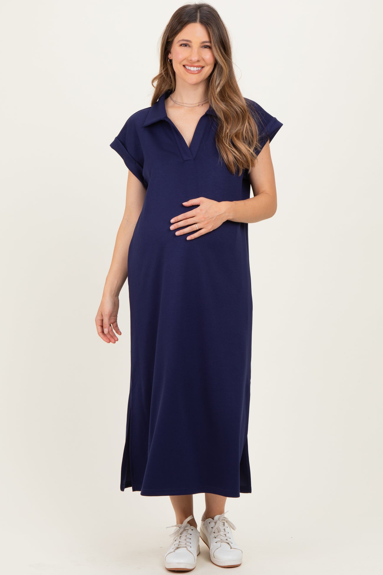 woman wearing a navy blue maternity dress with a polo collar and side slits, holding her baby bump