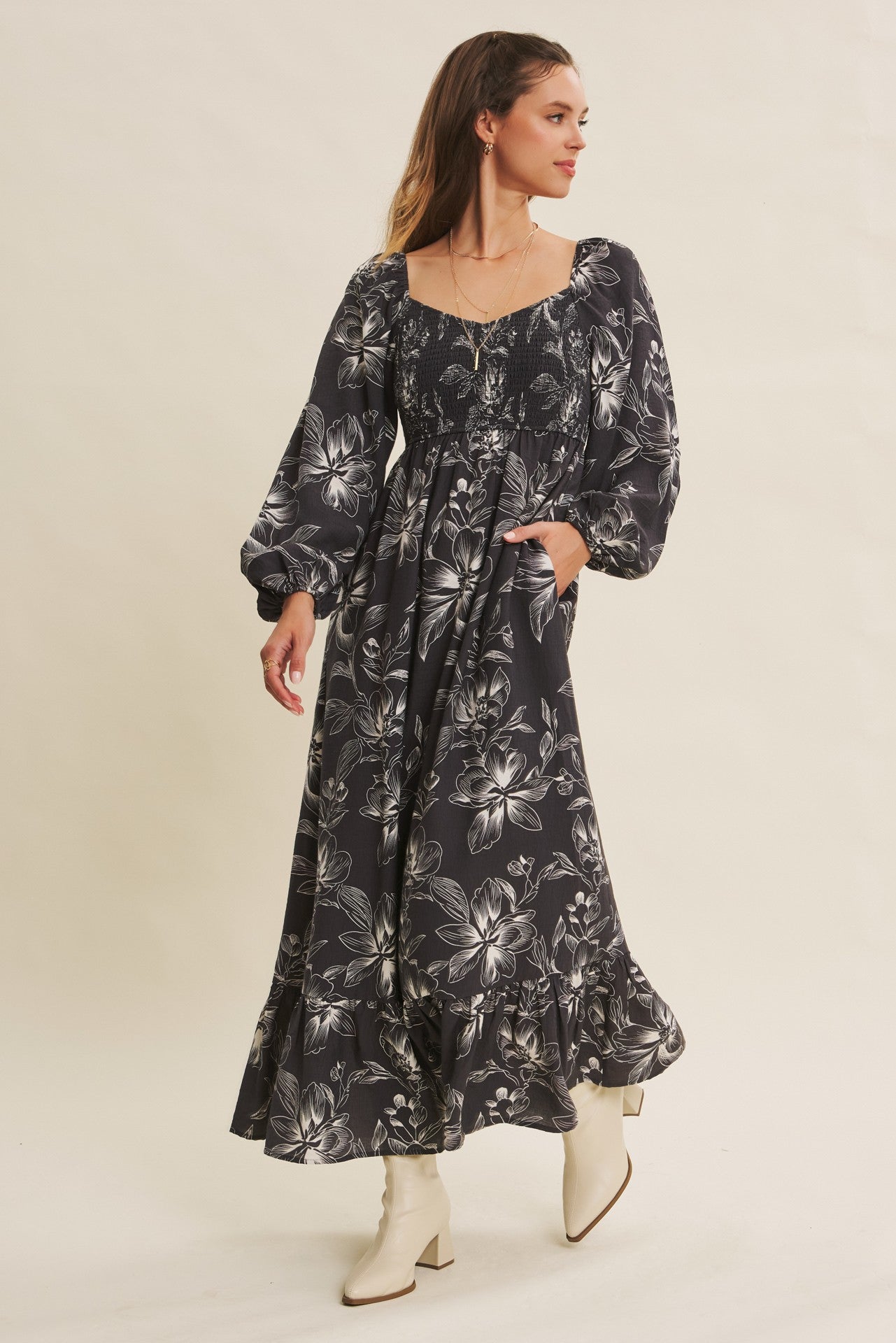 woman wearing a black floral maxi dress with puff sleeves and a tiered hem, posing with hands in pockets