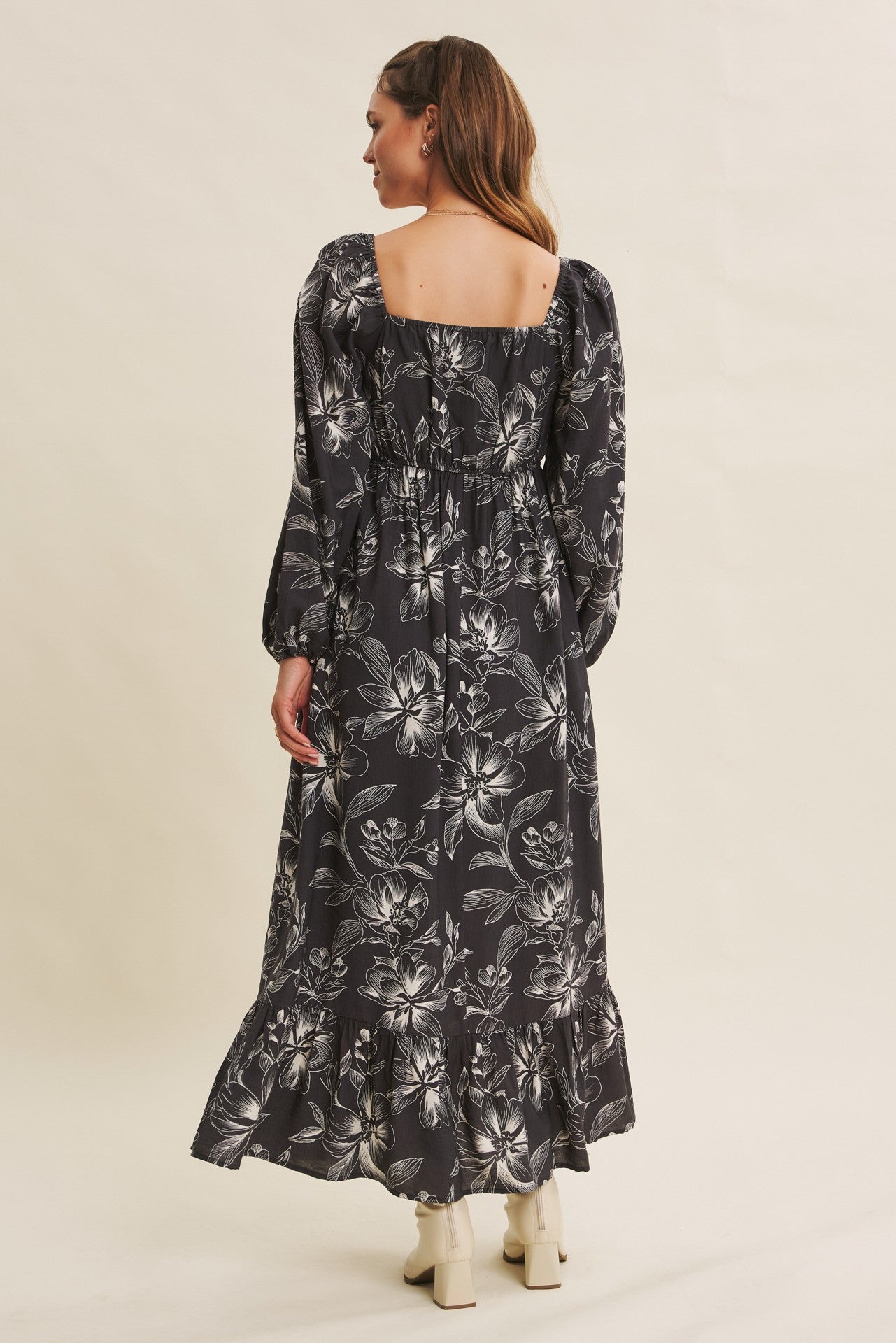woman wearing a black floral maxi dress with puff sleeves and a ruffled hem, viewed from the back