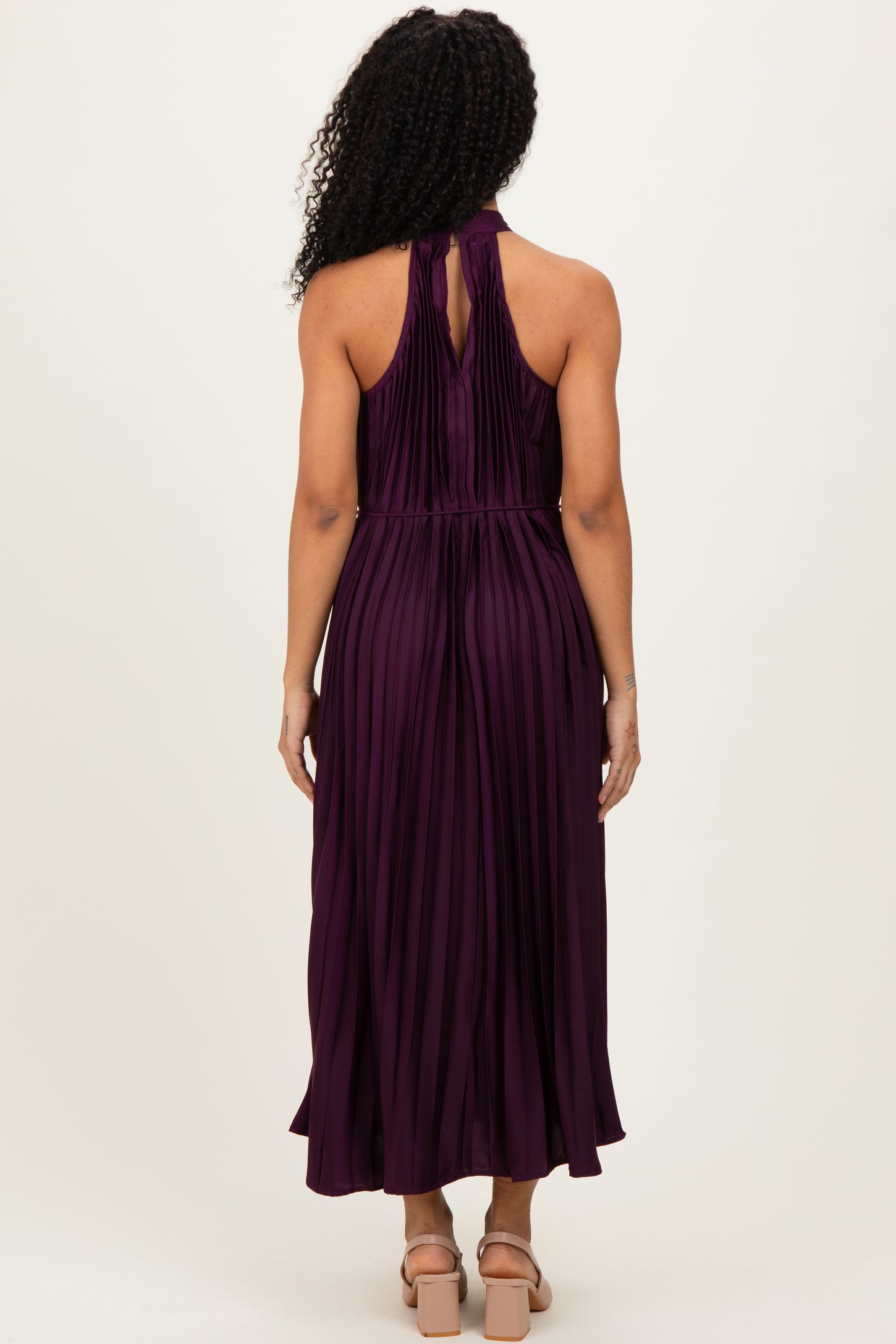 woman wearing a purple pleated halter neck maxi dress, showing the back view with a keyhole detail and flowy hem