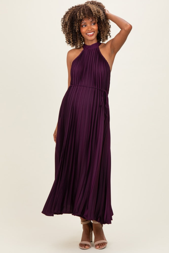 woman wearing a dark purple pleated maternity dress with a halter neckline and a tie at the waist, showcasing her baby bump