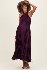 woman wearing a dark purple pleated maternity dress with a halter neckline and a tie at the waist, showcasing her baby bump