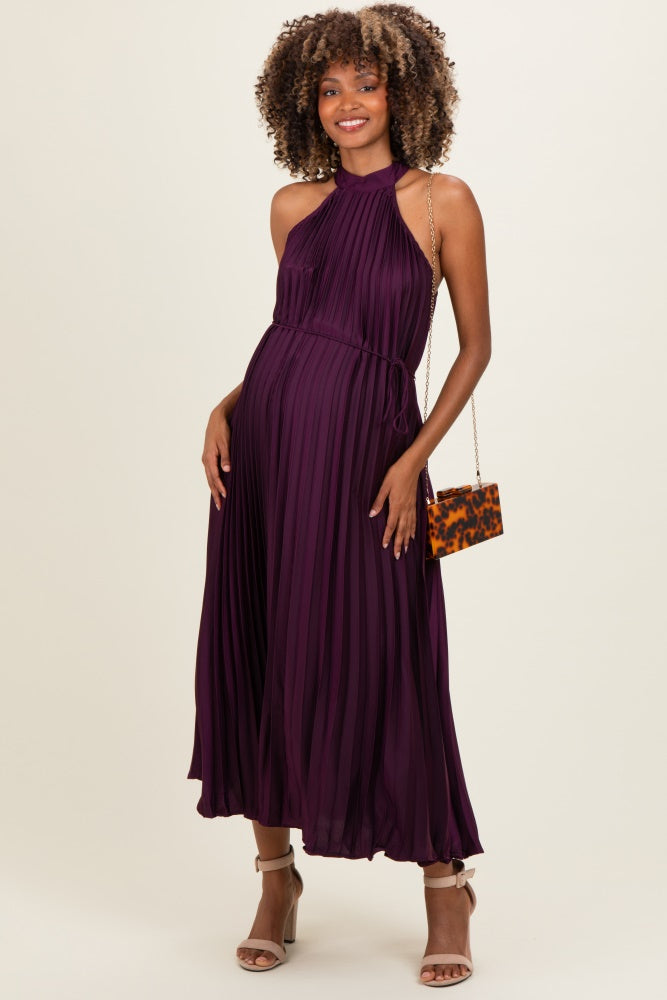 woman wearing a deep purple pleated maternity dress with a halter neck and holding a small purse, showing her baby bump