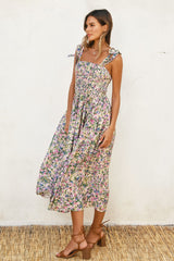 woman wearing a floral midi dress with shoulder ties and a smocked bodice, standing against a textured wall