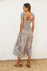 woman wearing a floral midi dress with tie straps and a smocked back, standing against a textured wall