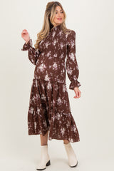 woman wearing a brown floral print maternity dress with long sleeves and a tiered skirt, showing her baby bump