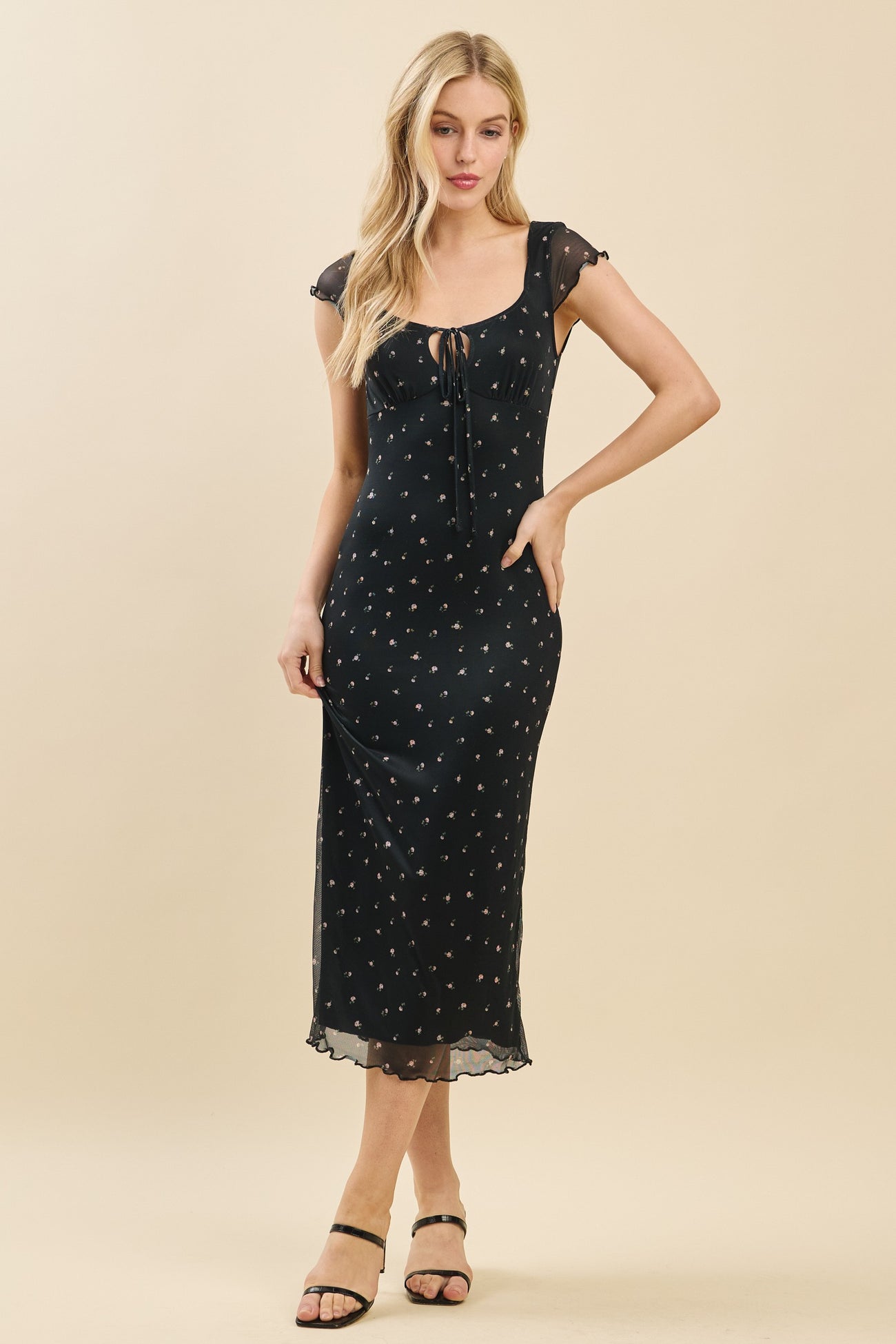 woman wearing a black midi dress with floral print and a lace-up neckline, standing in a relaxed pose