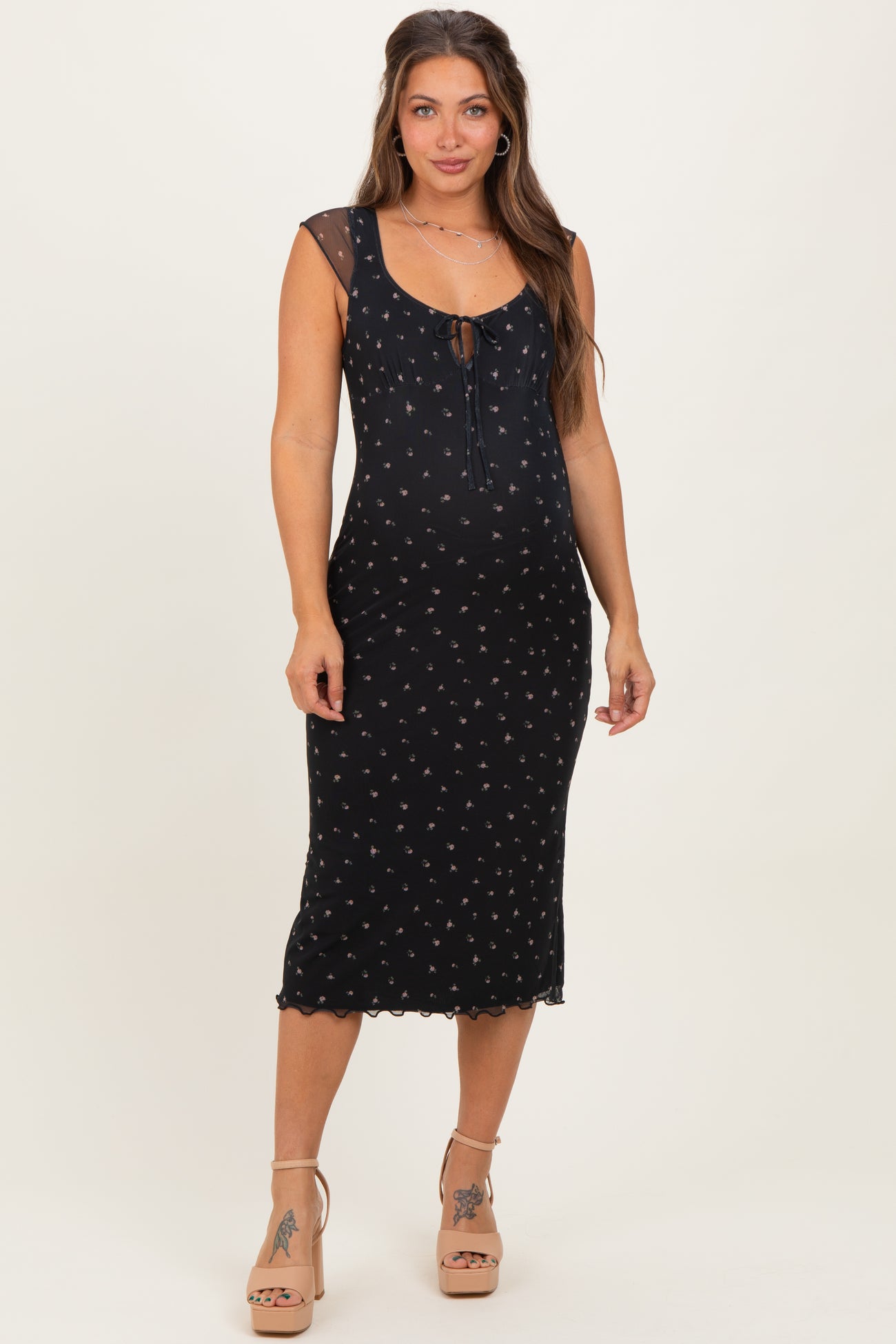 woman wearing a black floral maternity dress with a tie front, showcasing her baby bump and styled with nude heels