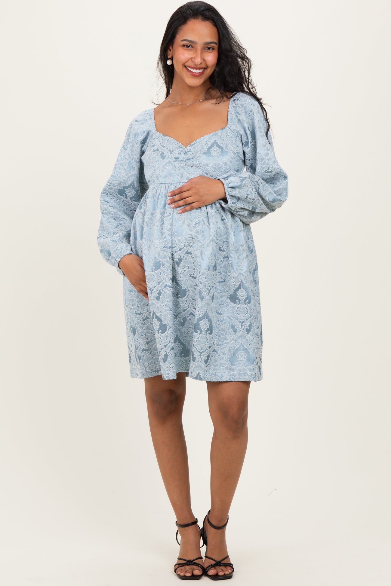woman wearing a light blue patterned maternity dress with a square neckline and long sleeves, holding her baby bump