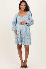 woman wearing a light blue patterned maternity dress with a square neckline and long sleeves, holding her baby bump