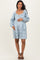 woman wearing a light blue patterned maternity dress with a square neckline and long sleeves, holding her baby bump