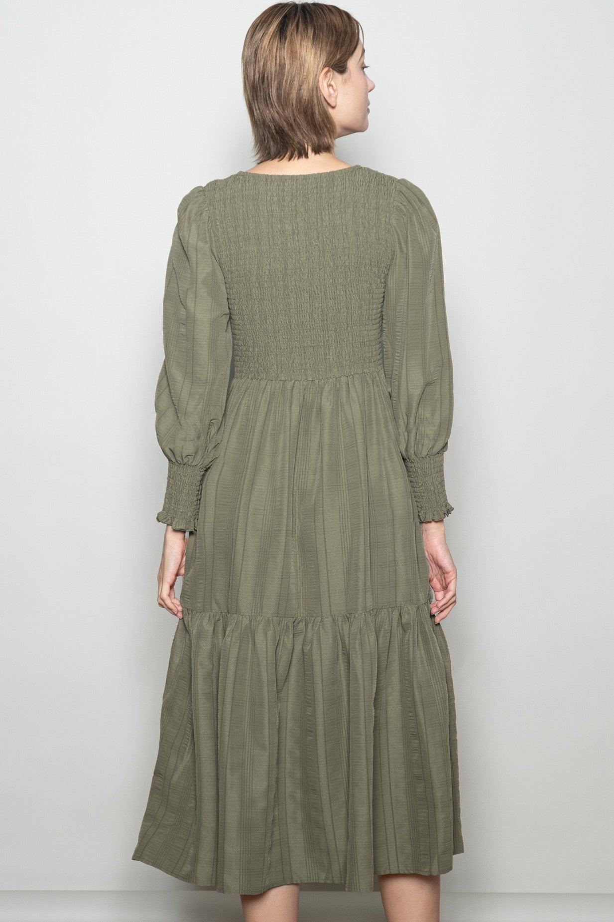 woman wearing an olive green smocked back midi dress with long puff sleeves and a tiered skirt