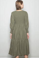 woman wearing an olive green smocked back midi dress with long puff sleeves and a tiered skirt