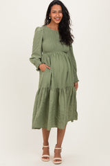 woman wearing a dark green long sleeve maternity dress with a flared skirt and pockets, showing her baby bump