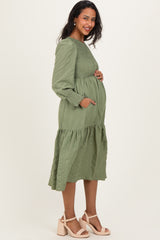 woman wearing a long sleeve sage green maternity dress with a smocked bodice and tiered skirt, showing her baby bump